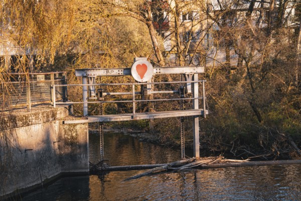 Dam with heart symbol in front of an autumnal riverbank, Stadtgarten Pforzheim, Germany