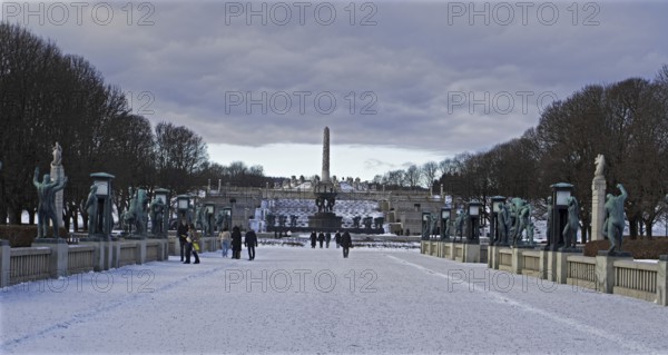 Snowy park (Vigeland Sculpture Park) with sculptures and walkers under a cloudy sky, Oslo Norway