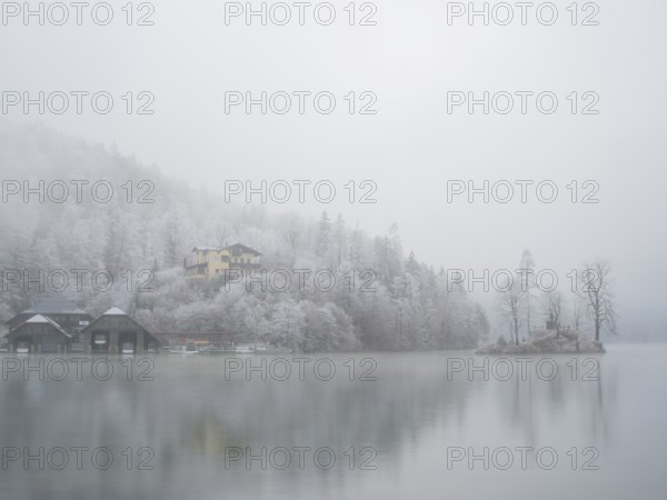 View across Königssee to boathouses, Christlieger island and frozen trees in fog, Schönau am