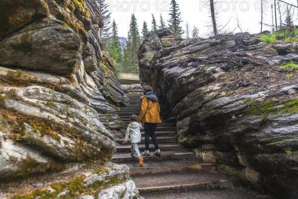 Mother and child walking up stairs among rocks and trees at athabasca falls in jasper national