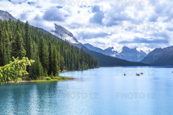 Tourists canoeing on turquoise maligne lake, surrounded by pine forests and snow capped mountains,