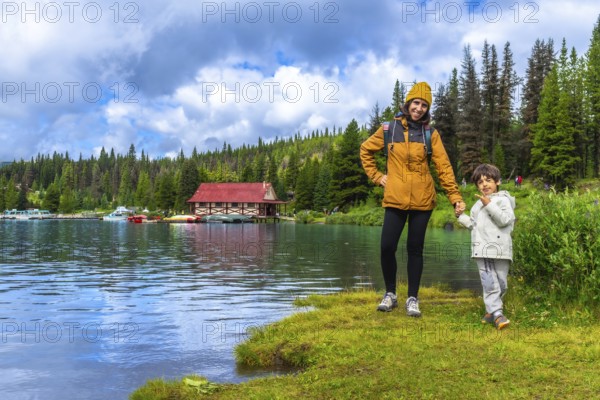 Mother and son holding hands, enjoying a scenic view of maligne lake boathouse in jasper national