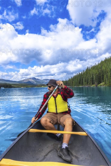 Tourist wearing sunglasses and life jacket paddling a canoe on beautiful maligne lake in jasper