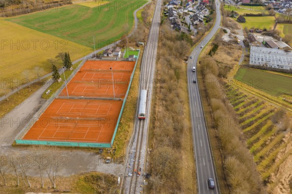 Aerial view of a landscape with railway tracks, tennis courts and roads, surrounded by fields and