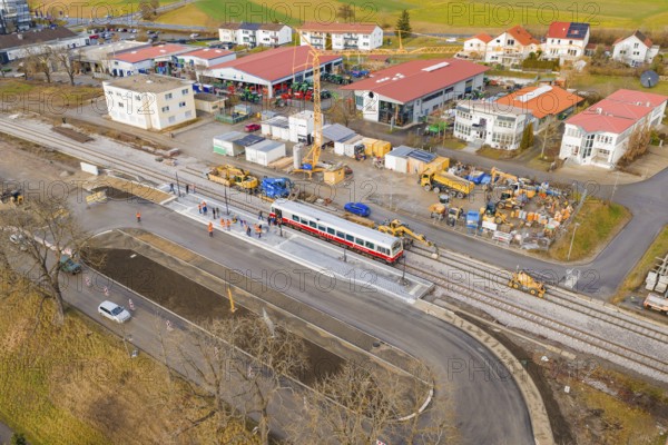 Workers and machines are working on an extensive construction site near tracks and a passing train,