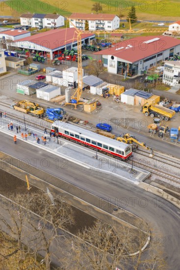 A train passes a large construction site with workers and a crane, historic event, first test run