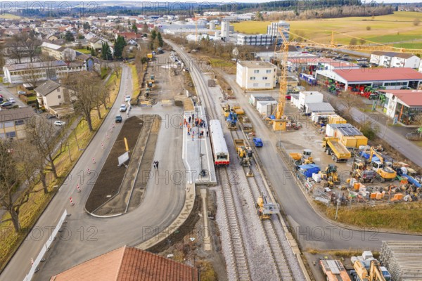 A few houses and a construction site at a municipal train station with train and construction work,