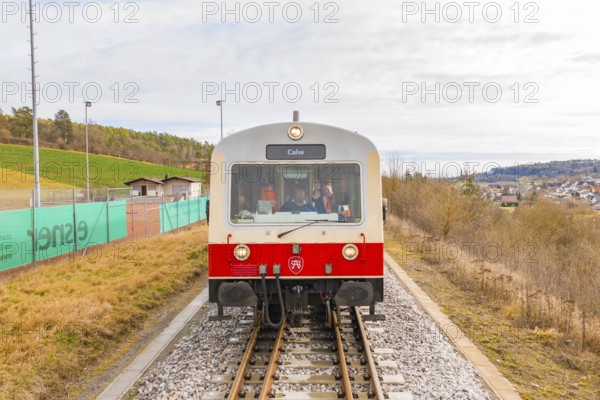 Train with passengers and the inscription 'Calw' on the rails, with landscape in the background,