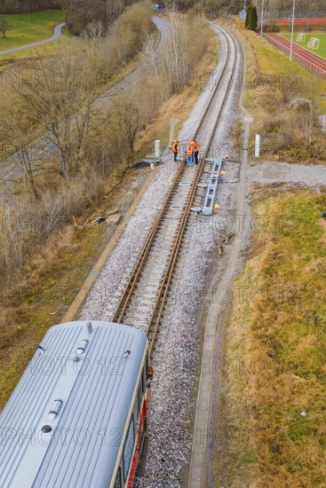 View along the railway tracks with a train and several construction workers on the rails, historic