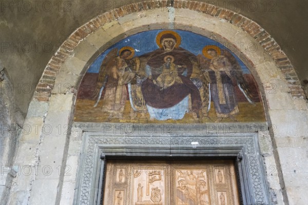 Fresco depicting Mary and Child Jesus and angels in a round arch above a decorated door,