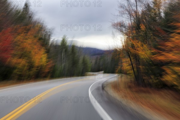 Winding country road through forest, autumn leaves, Indian summer, dark rain clouds, smudge effect,