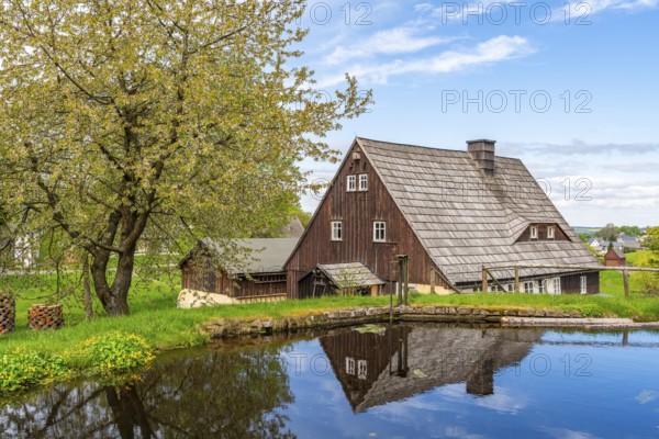 Historic houses with half-timbered timber and shingles on a pond under trees in the Seiffen