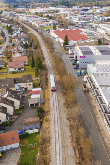 Train travels through a suburb with residential buildings and industrial buildings, surrounded by