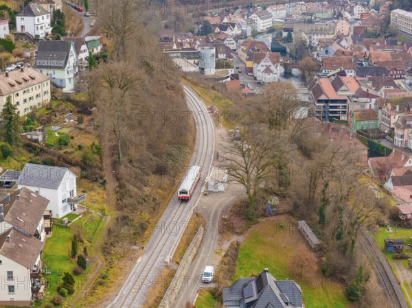 Train on railway line between town houses nestled in hilly, wooded landscape, historic event, first