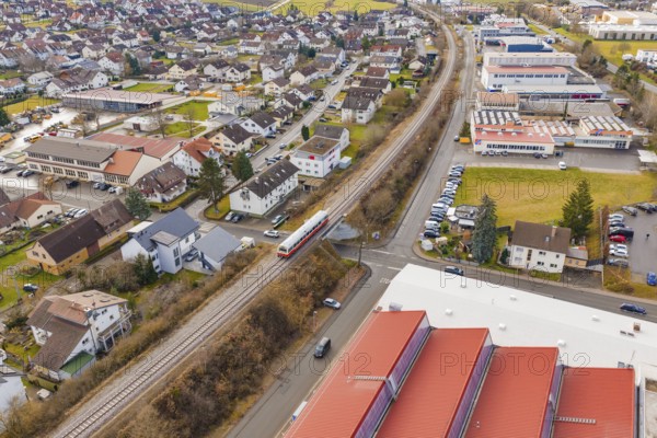 Train travels in a suburban landscape between residential buildings and industrial buildings,