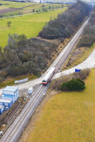 Train travels through a rural landscape with small infrastructures and surrounded by fields,