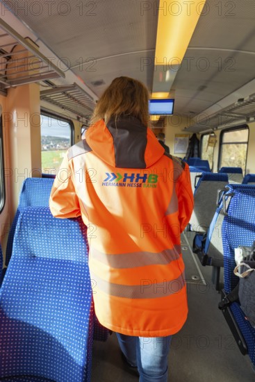 Person wearing safety clothing in the passenger area of a train, blue seat cover and looking