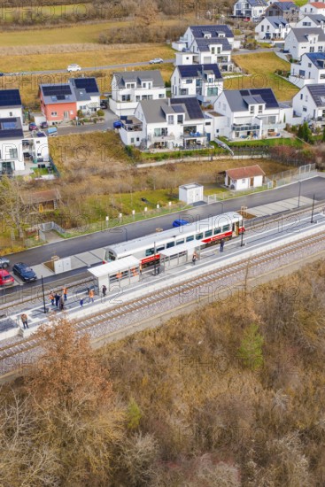 Train stops at a small train station next to modern houses surrounded by fields, historic event,