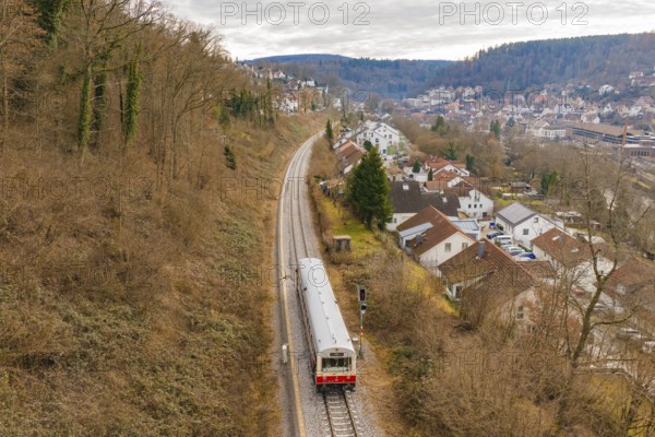 A train moves through a picturesque landscape with houses and hills in the background, historic