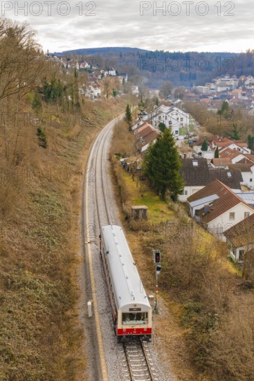 A train travels through a hilly landscape with houses and autumn trees, historical event, first