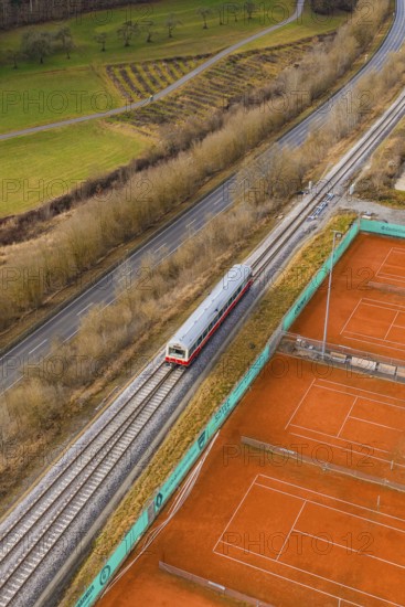A train travels through rural landscape next to orange tennis courts on railroad tracks, historic