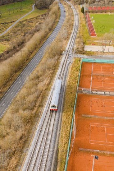 Railway tracks run next to tennis courts and a path in a wintry landscape, historic event, first