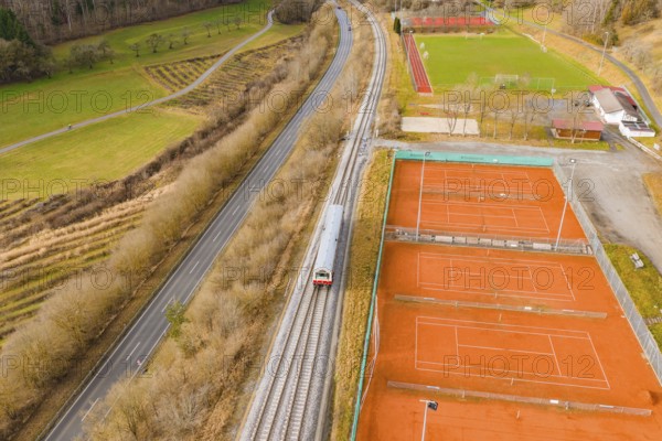 Train travels along tennis courts and green areas, autumn landscape with road and trees in the