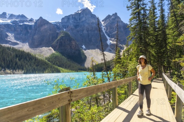 Female tourist walking along a wooden path, admiring the stunning turquoise waters of moraine lake