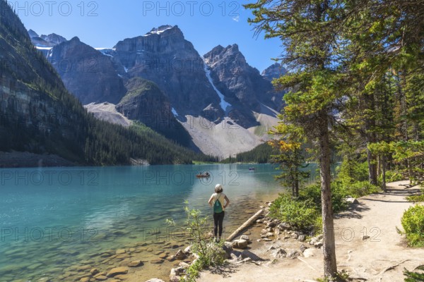 Female tourist standing on the shore of the turquoise moraine lake, admiring the canadian rockies