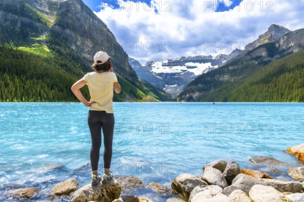 Tourist standing on rocks at the edge of vibrant turquoise waters of lake louise, admiring majestic
