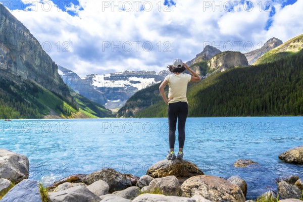 Tourist standing on rocks by the turquoise water of lake louise admires the surrounding canadian