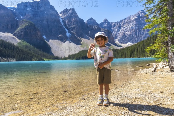 Young boy waving on the shore of moraine lake with the canadian rockies in the background, enjoying