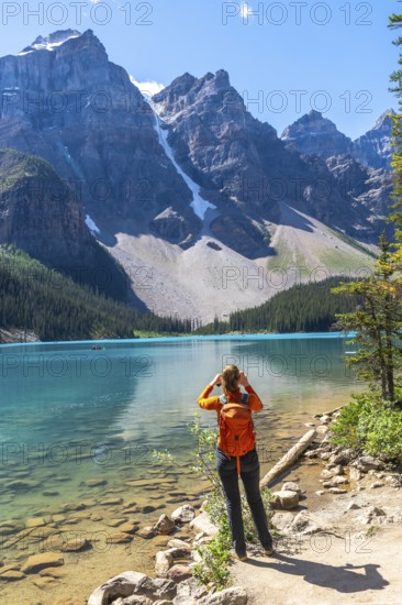Female tourist with backpack taking pictures of the turquoise waters of moraine lake and the