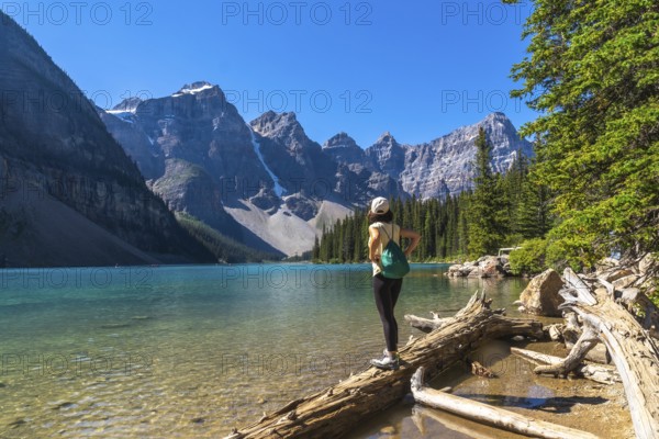 Female tourist standing on a log admiring the turquoise waters of moraine lake with the valley of