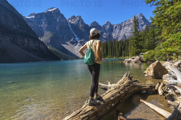 Female tourist standing on a log and admiring the turquoise waters of moraine lake, framed by the