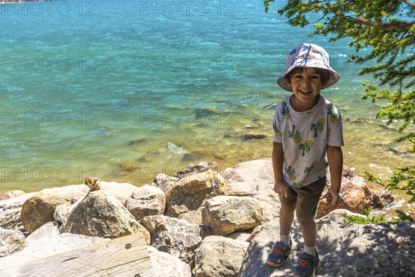 Happy child wearing a bucket hat standing by the turquoise water of moraine lake with a chipmunk