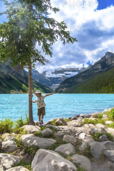 Young tourist balancing on rocks by a tree near the turquoise waters of lake louise, with snow