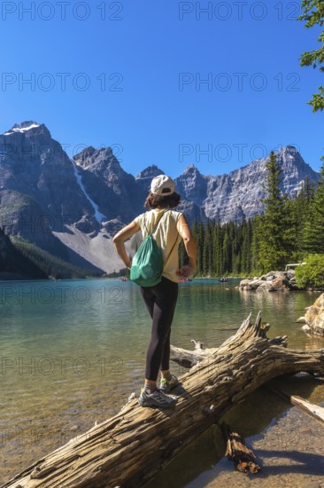 Female tourist standing on a log, admiring the turquoise waters of moraine lake, surrounded by the