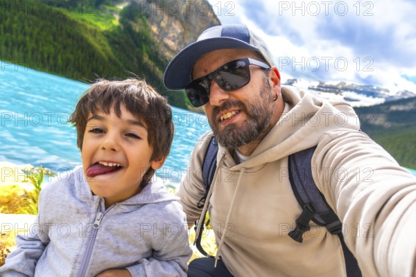 Father and son capturing a selfie by the turquoise waters of lake louise, surrounded by stunning