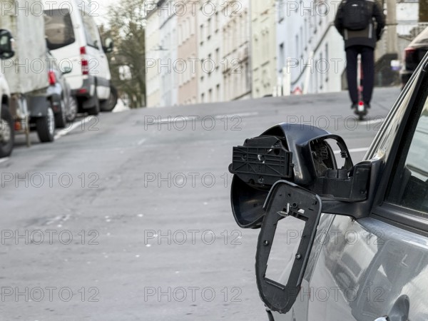 A car on the side of a steep residential street. The vehicle's left wing mirror is severely damaged