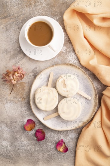 ?hocolate Ice cream in white glaze, cup of coffee, on brown concrete background and orange textile,