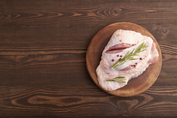 Raw Turkey Thigh with spices and rosemary on cutting board on brown wooden background. top view,
