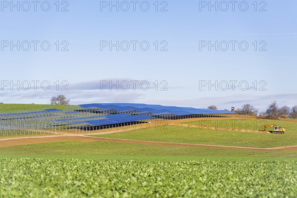 A tractor works in a field with installed solar panels under a blue sky, Energiewende, construction