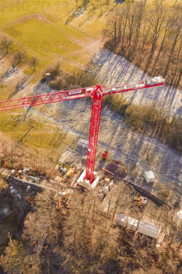 Red crane seen from the air on a construction site on the edge of a forest in an autumn landscape,