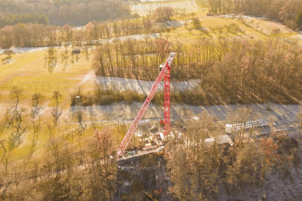 Crane dominates construction site in autumn landscape, surrounded by forests and meadows,