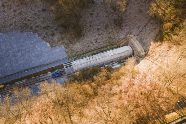 A train emerges from a tunnel located in a forested and frosty environment, construction of the