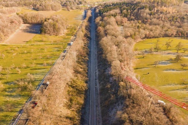 A railway cuts through fields and forests in a wintry countryside landscape, construction of the