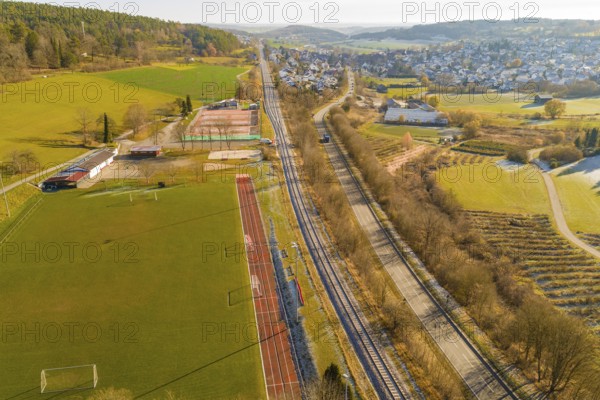 Aerial view of a railway bordering fields and a sports field in a rural area, construction of the