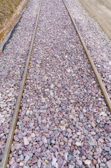Detailed view of railroad tracks densely covered with grey and purple gravel, construction of the