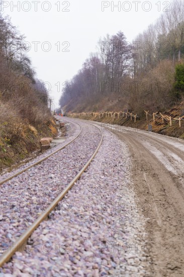 Railway tracks wind their way through a wooded, quiet landscape under cloudy skies, built by the